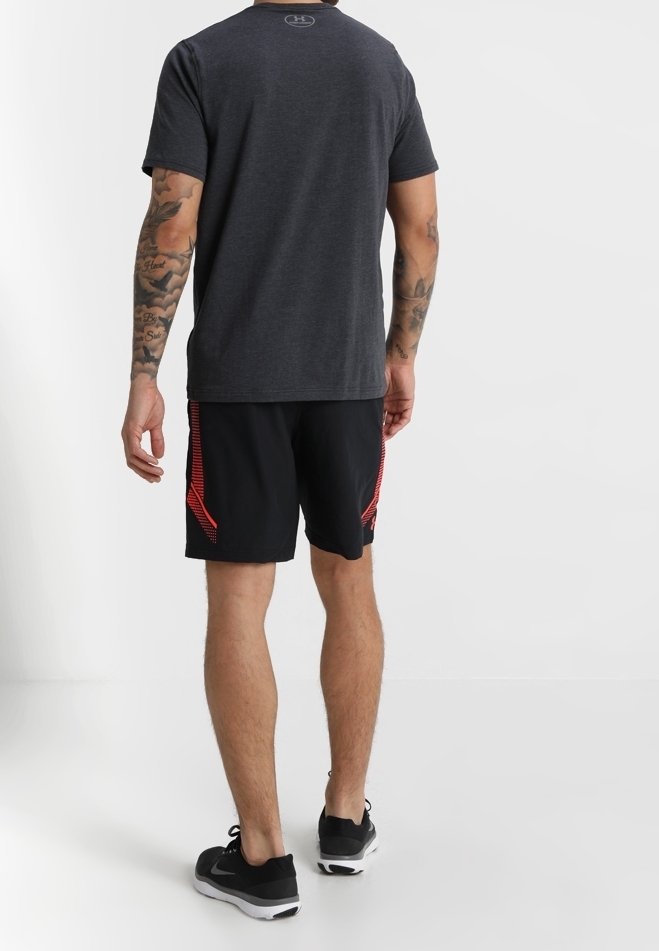 Šedé tričko s krátkým rukávem a kulatým výstřihem, spárované s černými šortkami s červenými bočními detaily a hladkou texturou. Černé sportovní boty.