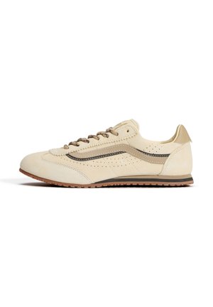 Beige low-top sneaker med ruskindstekstur, perforerede sidepaneler, brune snørebånd, brun og sort sideliste og gummisål.