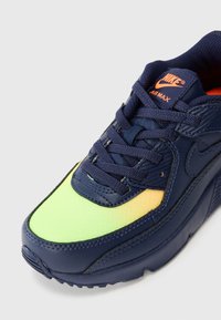 Nike Air Max tenisice imaju gornji dio od tamnoplavog kože i mrežaste tkanine, neonske žute i zelene akcentne boje, te teksturiranu gumenu potplatu.