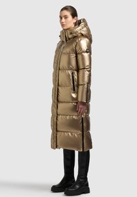 Cappotto imbottito metallizzato color oro fino al ginocchio con cappuccio, caratterizzato da trapuntatura orizzontale, tasche laterali con zip e dettagli neri.