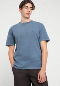 T-shirt en coton bleu avec un col rond et des manches courtes. Présente un petit logo sur la poitrine gauche. Texture lisse et coupe décontractée.