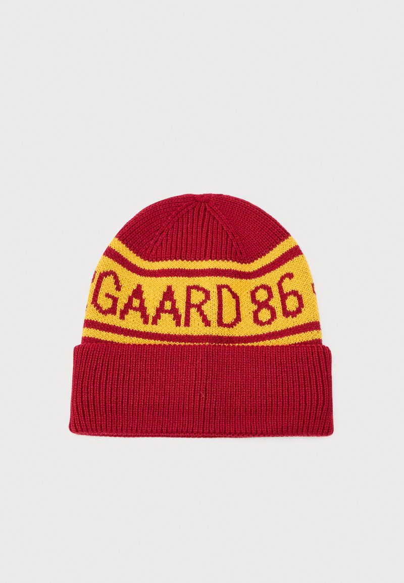 Bonnet en tricot rouge avec des rayures jaunes et un motif "GAARD 86". Il présente un revers retroussé et une finition tricotée texturée.