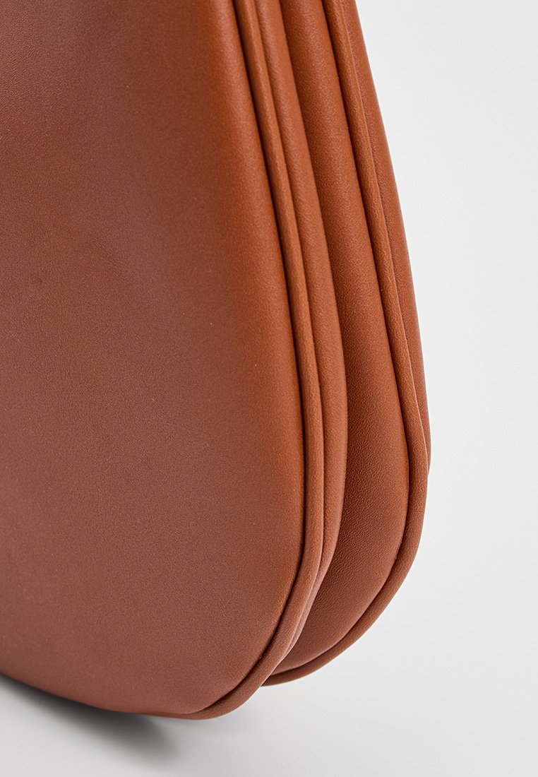 Braune synthetische Handtasche mit glatter Textur, runder Form und gefaltetem Design, das subtile Nähte für Dimension bietet.