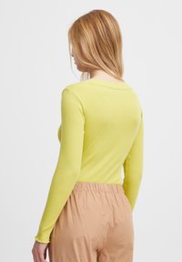 Langärmliges Oberteil aus leuchtend gelbem Rippstoff mit rundem Ausschnitt und schmaler Passform. Kombiniert mit hellbeigen, elastischen Bundhosen.