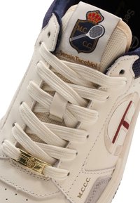 Pantof sport bej și alb cu partea superioară din piele texturată, accente albastre contrastante, șireturi plate, un accent auriu și detaliu cu logo brodat.