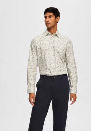 Camisa de manga larga con un patrón floral en verde claro sobre un fondo blanco. La tela es suave, con un collar abotonado y mangas con puños.