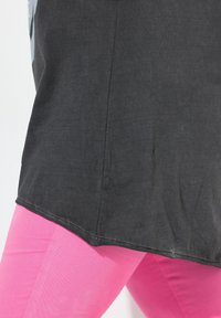 Zwarte, gestructureerde tuniek met een ronde zoom, gecombineerd met felroze leggings, die een gladde stof en een getailleerd ontwerp laten zien.