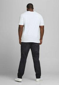 White short-sleeve t-shirt, relaxed fit, paired with dark denim jeans. The model is facing away, with simple white sneakers visible.