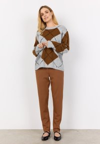 Maglione grigio con rombo marrone e dettagli a motivo nero, abbinato a pantaloni marroni a gamba stretta e ballerine nere. Tessuto morbido.