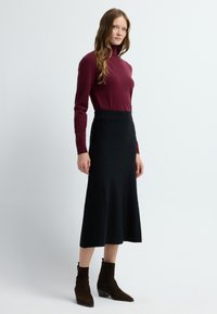 Bordeaux lange mouwen strakke top gecombineerd met een zwarte uitlopende midi-rok en donkerbruine enkellaarzen met een kleine hak. Gladde, minimalistische textuur.