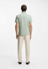 Hellgrünes Poloshirt mit kurzen Ärmeln und Kragen, kombiniert mit cremefarbenen Hosen, von hinten betrachtet. Flache Textur, minimale Details.