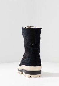 Bota de ante azul marino con un forro suave de color claro. Presenta una suela de goma blanca gruesa y un contraste de costuras azules a lo largo de las costuras.