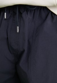 Pantalons navy avec taille élastique et cordon de serrage réglable, dotés d'un tissu lisse et léger avec une texture subtile.