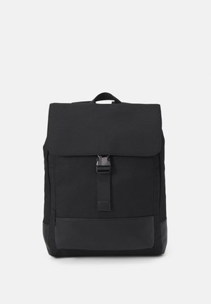 Sac à dos rectangulaire noir avec un rabat avant sécurisé par une boucle centrale et une poignée de transport en haut, sur un fond uni.
