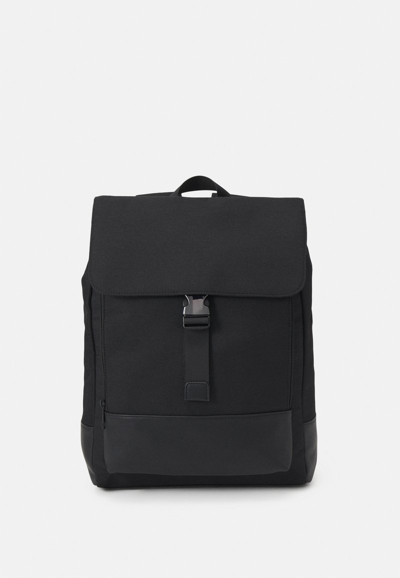 Sac à dos rectangulaire noir avec un rabat avant sécurisé par une boucle centrale et une poignée de transport en haut, sur un fond uni.