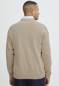 Beige gestrickter Pullover mit gerippten Bündchen und Saum, in lässiger Passform und mit einfarbiger Textur, von hinten gezeigt.
