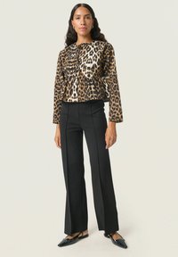 Veste cropped en imprimé léopard avec un design à peplum, accompagnée de pantalons noirs ajustés et de ballerines noires à bout pointu. Tissu lisse et manches longues.