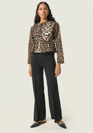 Leopardenmuster cropped Jacke mit einem Peplum-Design, kombiniert mit taillierten schwarzen Hosen und schwarzen spitzen Ballerinas. Glattes Material und lange Ärmel.