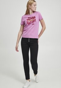 Camiseta de algodón rosa con estampado gráfico de flores, combinada con pantalones ajustados negros que tienen cinco botones y zapatillas blancas.