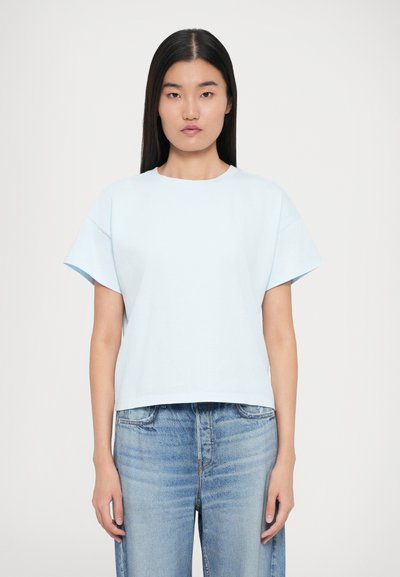 T-shirt court bleu clair en coton doux, avec des manches courtes et un encolure ronde, porté avec un jean bleu délavé.