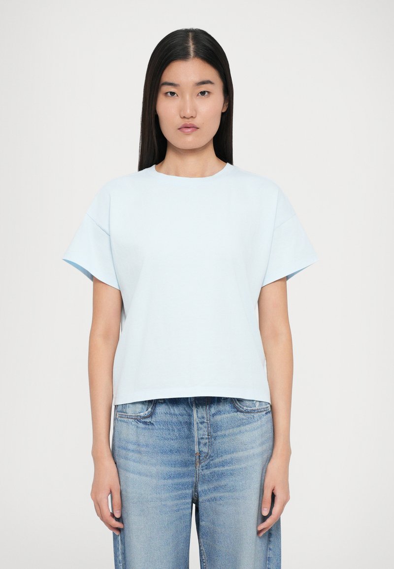 Lyseblå cropped t-shirt lavet af blødt bomuld, med korte ærmer og rund halsudskæring, parret med slidte blå jeans.