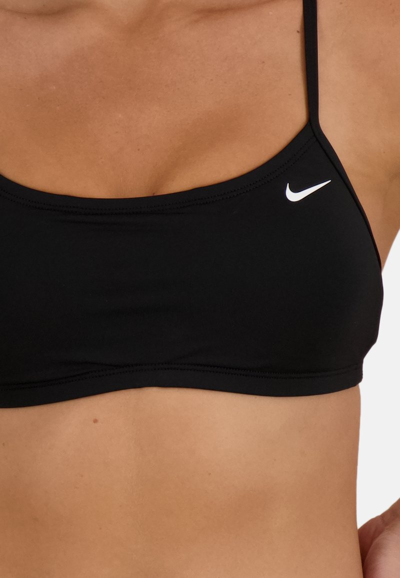 Czarny stanik sportowy z cienkimi ramiączkami, płaskimi szwami i białym logo Nike po lewej stronie. Gładki materiał o dopasowanym, strukturalnym kroju.