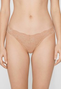 Spitzen-Tanga in Nude-Farbe mit floralem Muster. Mit zarter Einfassung am Bund und weicher, transparenter Textur.