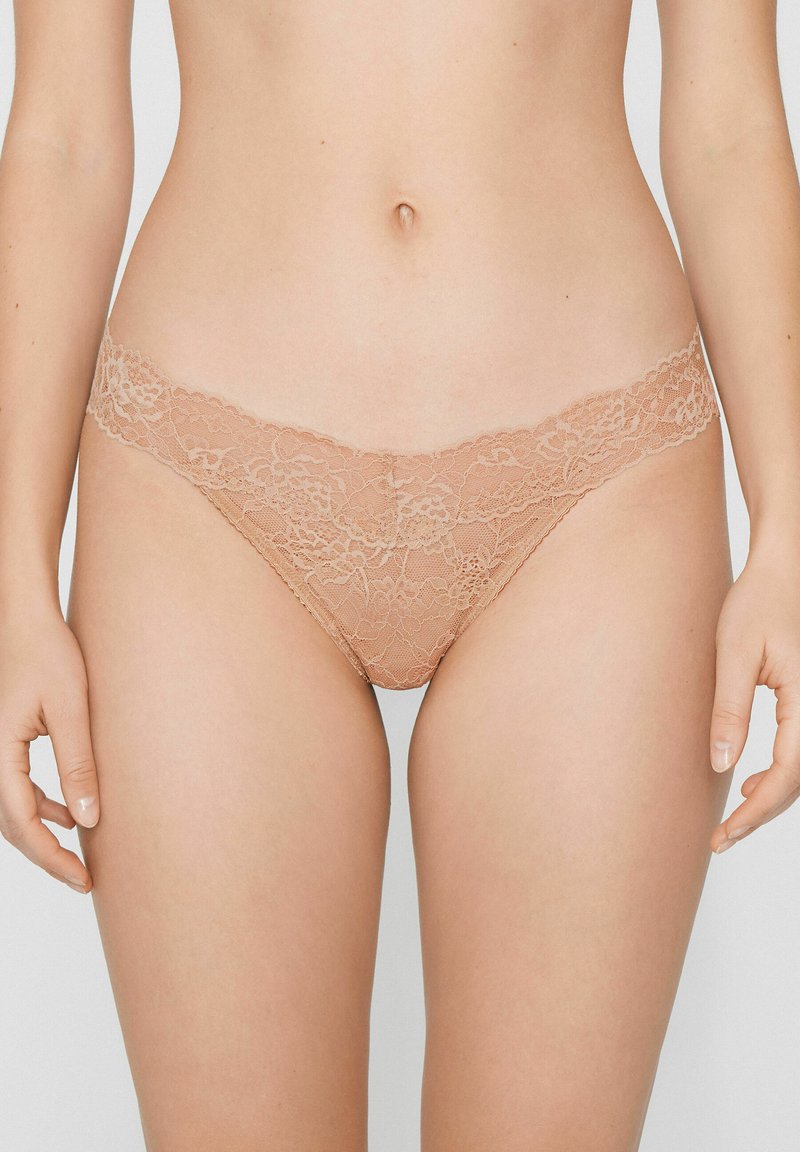 Spitzen-Tanga in Nude-Farbe mit floralem Muster. Mit zarter Einfassung am Bund und weicher, transparenter Textur.