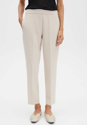 Beige op maat gemaakte broek met een gladde textuur, twee zakken aan de voorkant en een taps toelopende pasvorm. Draag ze met een zwarte top en lichte platte schoenen.