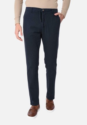 Pantaloni chino blu navy in cotone, con chiusura a zip e bottone, tasche laterali e vestibilità comoda. Indossati con scarpe slip-on marroni.
