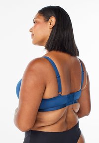 Blauwe gladde stoffen bh met verstelbare schouderbanden, haak-en-oog sluiting aan de achterkant en naadloze cups. Eenvoudig ontwerp en nauwe pasvorm.