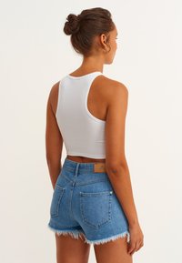 Vit ribbad linne kombinerat med blå denimshorts med fransade kanter och bakfickor. Outfiten har en avslappnad passform.