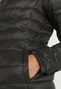 Kurtka puchowa w ciemnoszarym kolorze z pikowanymi panelami, elastycznymi mankietami i bocznymi kieszeniami. Wykonana z gładkiego, błyszczącego materiału zapewniającego ciepło.