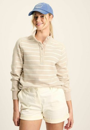 Beige striped long-sleeve shirt with button closure and rolled cuffs, paired with cream shorts. The cap is light blue with a logo.