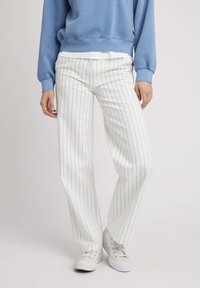 Pantalons blancs rayés avec des lignes bleues, présentant une coupe droite. Associés à des baskets blanches et un sweat-shirt bleu.