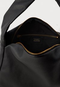 Μαύρη δερμάτινη τσάντα χειρός με υφή, διαθέτοντας χρυσό φερμουάρ και υφασμάτινη επένδυση στο εσωτερικό. Το εσωτερικό περιλαμβάνει μια τσέπη με φερμουάρ με επωνυμία.