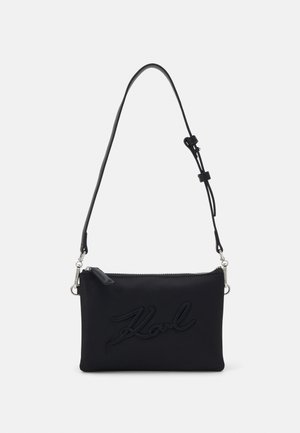 Sac bandoulière rectangulaire noir avec sangle réglable et fermeture éclair, avec logo en relief "Karl" sur le devant.