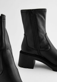 Black leather ankle boots with a side zipper, chunky heels, and textured rubber soles. Simple design with curved stitching detail.