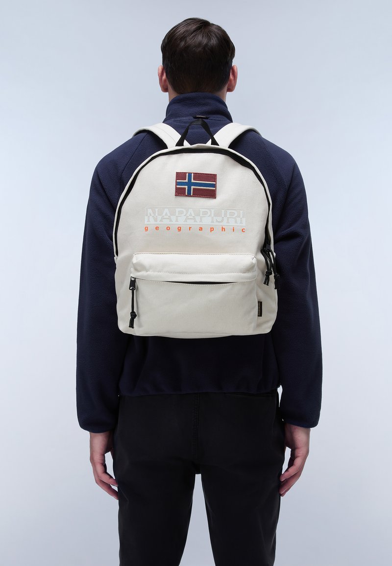 Bílý látkový batoh s černými akcenty, má nášivku norské vlajky, text "NAPAPIJRI geographic" a přední zipovou kapsu.