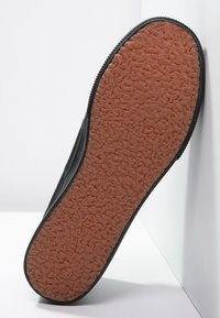 Semelle de chaussure noire avec une surface en caoutchouc texturée et un dessous marron à motif. Présente un bord lisse et des coutures renforcées sur les côtés.