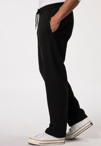 Zwarte sweatpants met een tailleband met trekkoord, zijzakken en een taps toelopend ontwerp. Gecombineerd met witte sneakers met rode accenten.