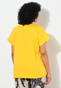 Camiseta amarilla de manga corta con un corte holgado y escote redondo, hecha de un tejido suave. La parte posterior presenta un diseño liso y minimalista.