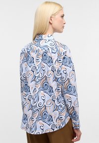 Blusa a maniche lunghe con un motivo a spirale blu, bianco e beige, realizzata in tessuto leggero con polsi abbottonati e colletto.