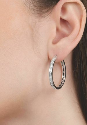 Close-up van een linker oor met een zilveren oorring bezet met kleine heldere edelstenen.