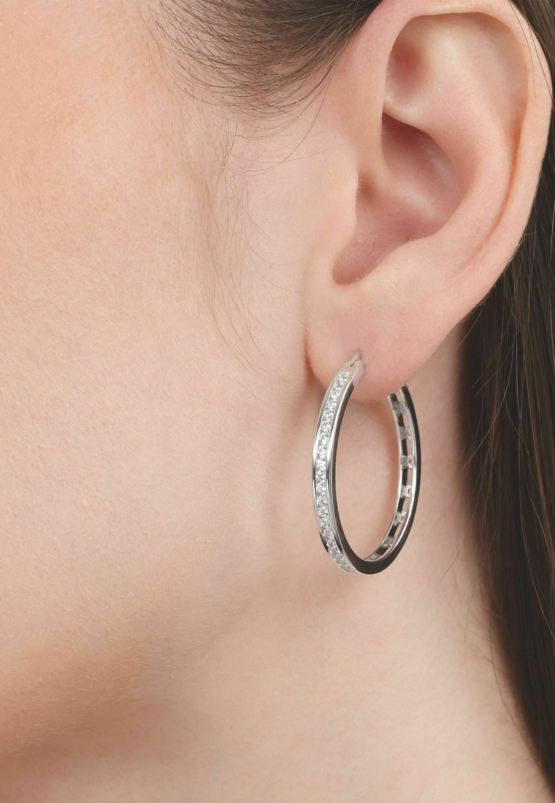 Primer plano de una oreja izquierda que lleva un pendiente de aro plateado incrustado con pequeñas piedras preciosas claras.