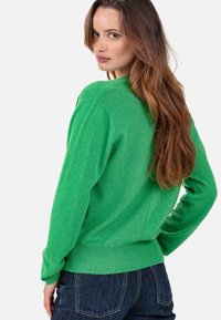Pull vert avec un col rond, des manches longues et un ourlet côtelé. Le tissu a une texture douce avec un motif chiné subtil.