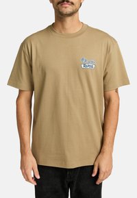 Tan korte mouwen t-shirt gemaakt van katoen met een ronde hals. Bevat een blauw logo en rozenafbeelding op het linker borstzakgebied.