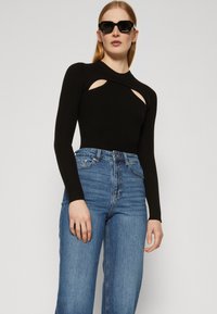 Μαύρο κορμάκι με ραβδωτή υφή και μακριά μανίκια, με λεπτομέρειες κοπής στο στήθος και συνδυασμένο με ανοιχτόχρωμες τζιν ψηλόμεσες παντελόνες. Λείο υλικό.