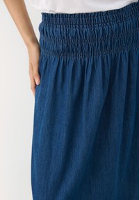Denim maksi krilo z nabranim elastičnim pasom, v globoko modri barvi, s povezano teksturo in tekočim materialom.