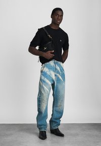 Černé tričko s krátkým rukávem a malým emblémem, oprané světle modré džíny s tie-dye efektem a černé kotníkové boty. Černá kabelka přes rameno.